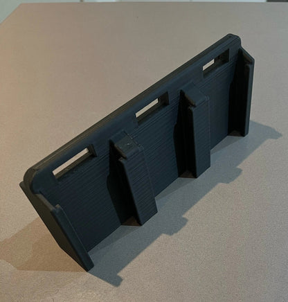 Makita 6-Slot Battery Holder designed for wall-mountable storage, showcasing a black organizer with three secure slots for 18V batteries on a sleek surface.