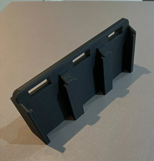 Makita 6-Slot Battery Holder designed for wall-mountable storage, showcasing a black organizer with three secure slots for 18V batteries on a sleek surface.