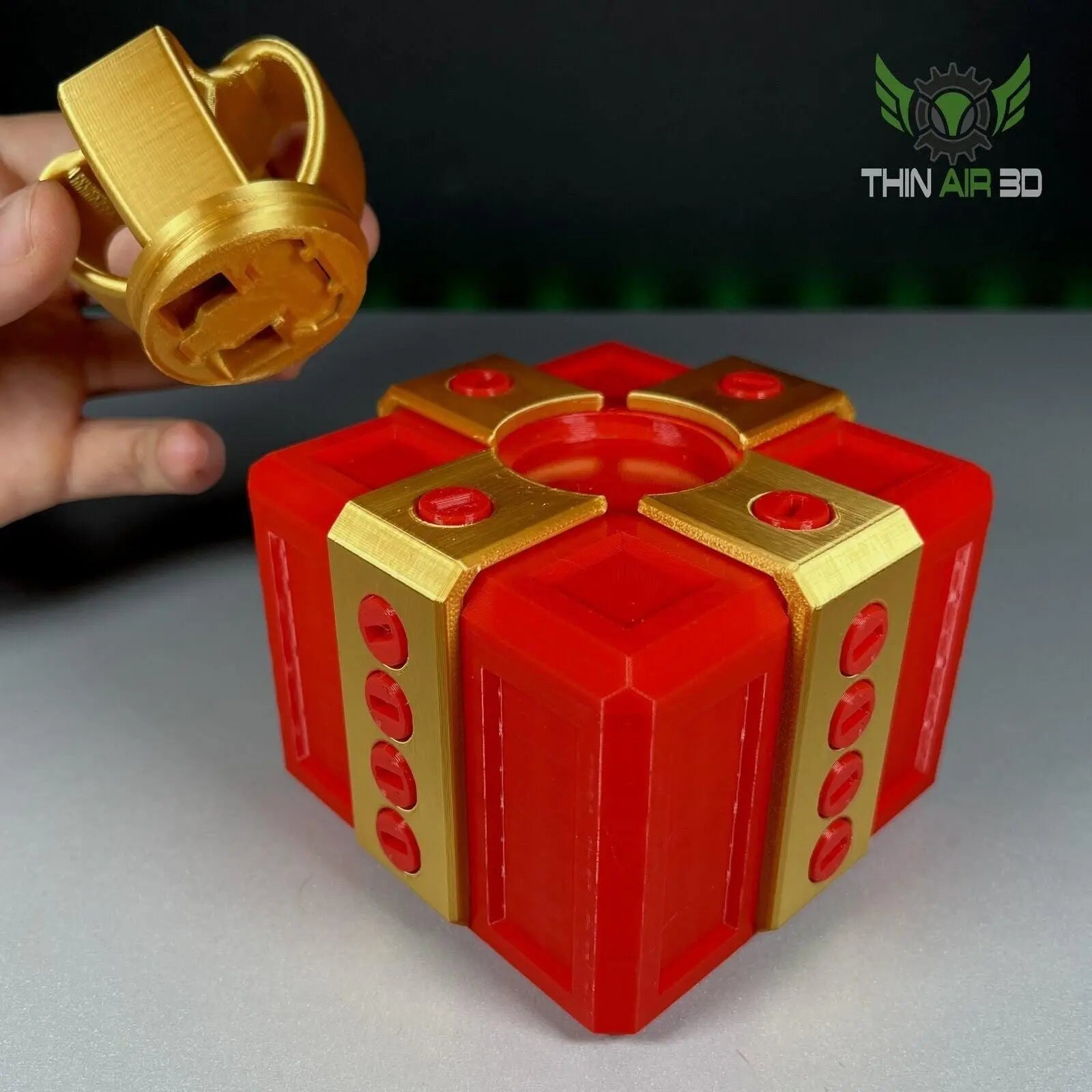 The Ultimate Challenge Gift Box held in hand, displaying a close-up of the vibrant red and gold design with a gold top piece being placed.